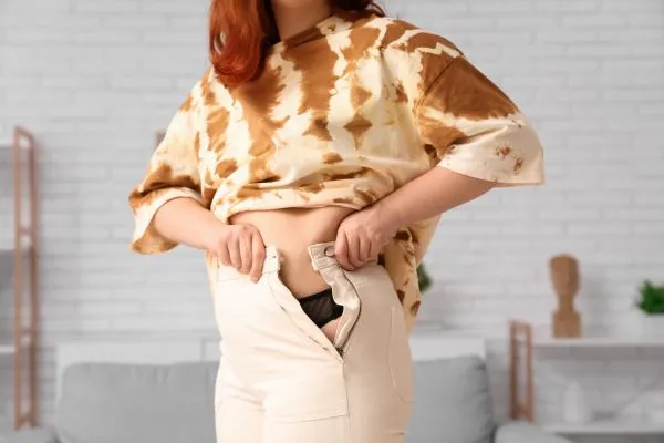 Image of woman trying to do her trousers up after pregnancy weight gain Bridge End