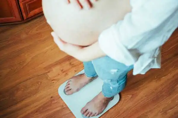 Image of woman weighing herself and experiencing weight gain through pregnancy Bridge End